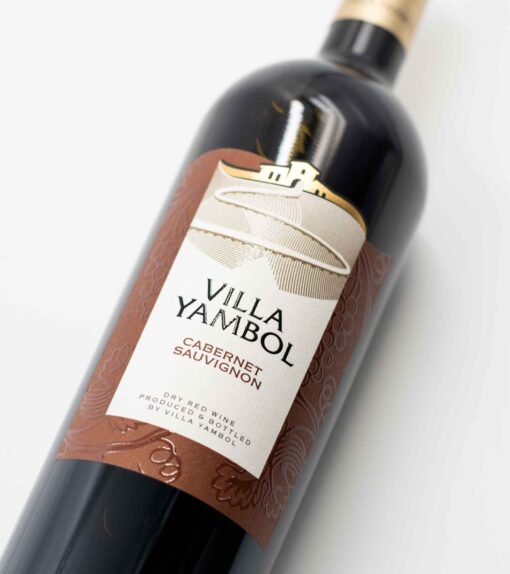 Detail fľaše bulharského vína Villa Yambol Cabernet Sauvignon so sýtym rubínovým odtieňom vína.